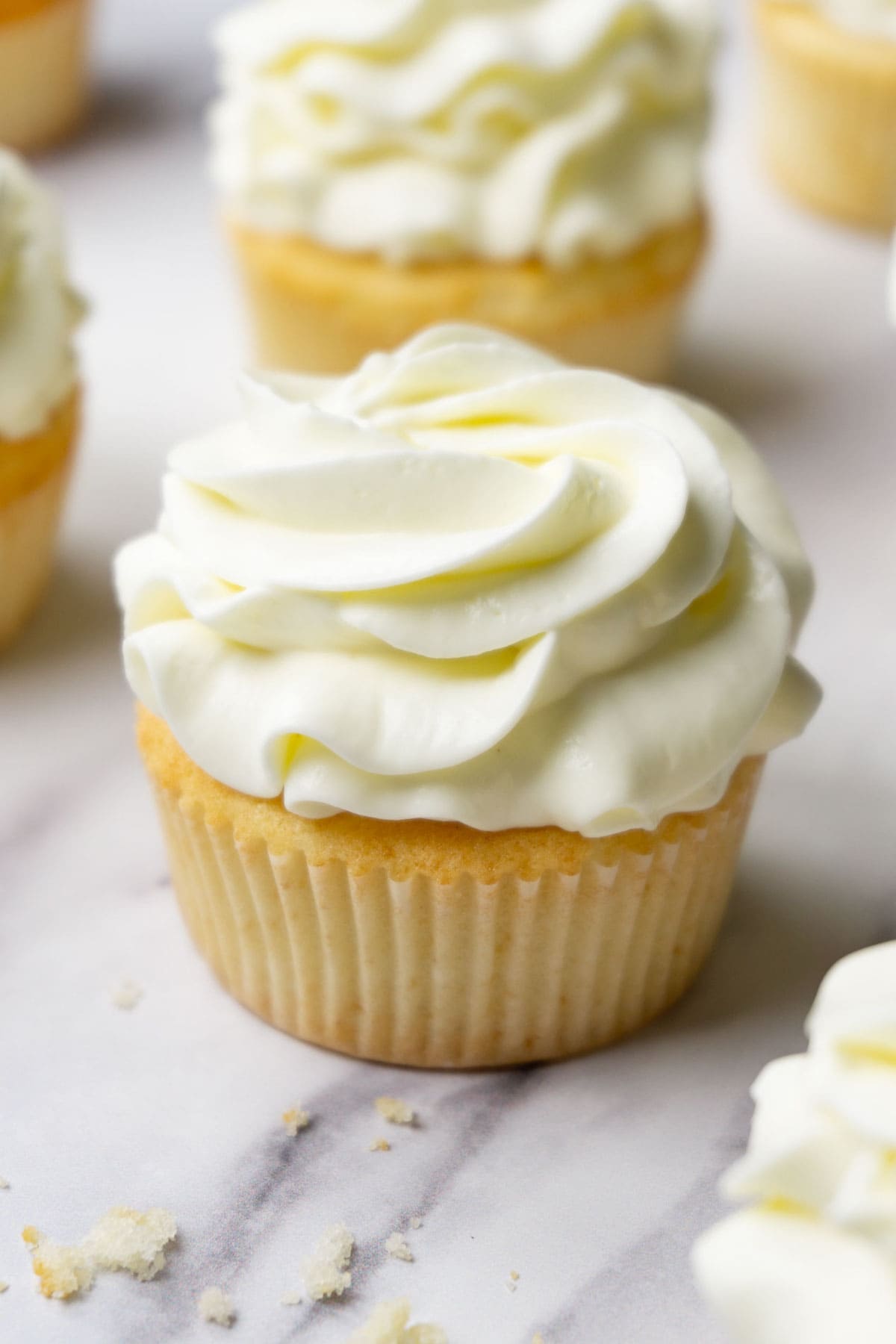 Vanilla cupcake with cream cheese frosting, more cupcakes are lying around.