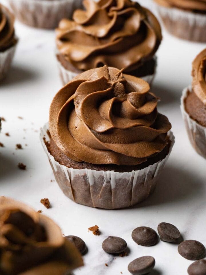 Chocolate cupcake with chocolate frosting, more cupcakes are lying around.