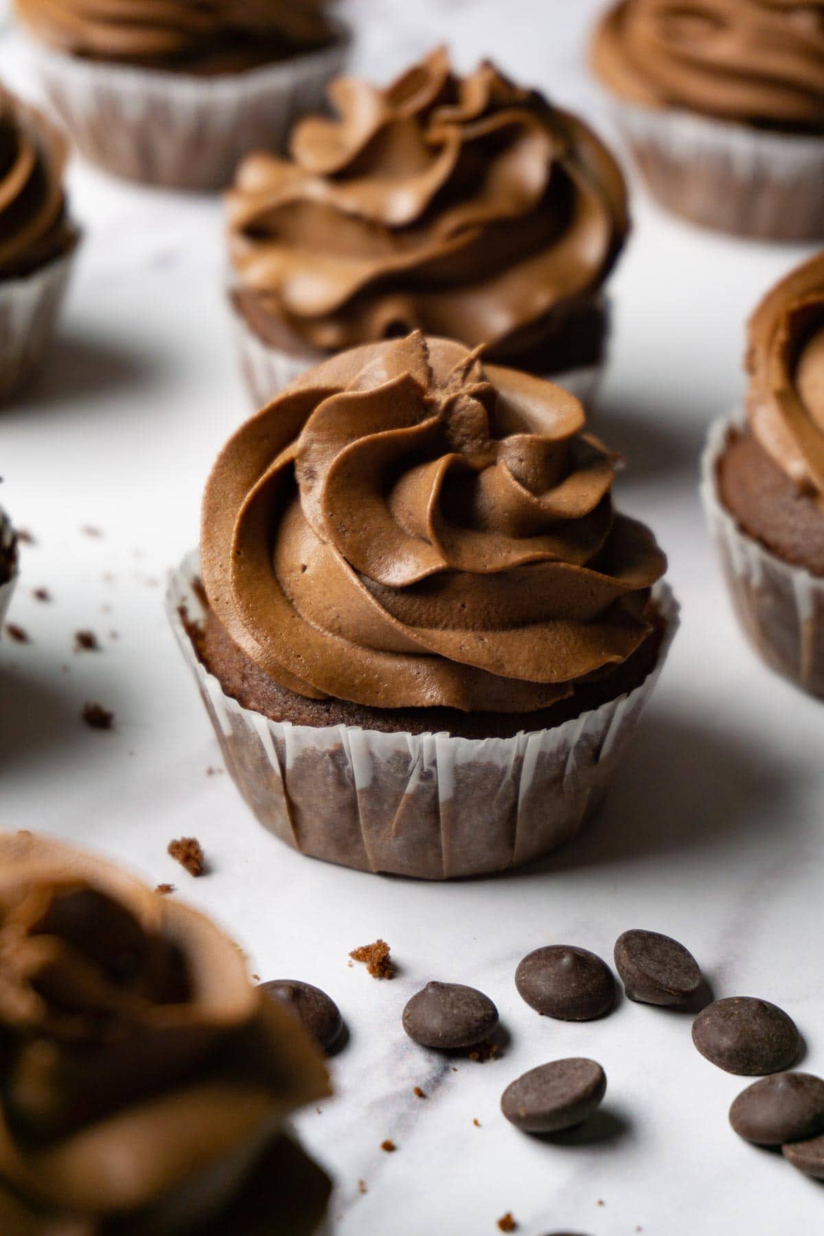 Chocolate cupcakes with chocolate frosting on a marble surface, chocolate chips are lying around.
