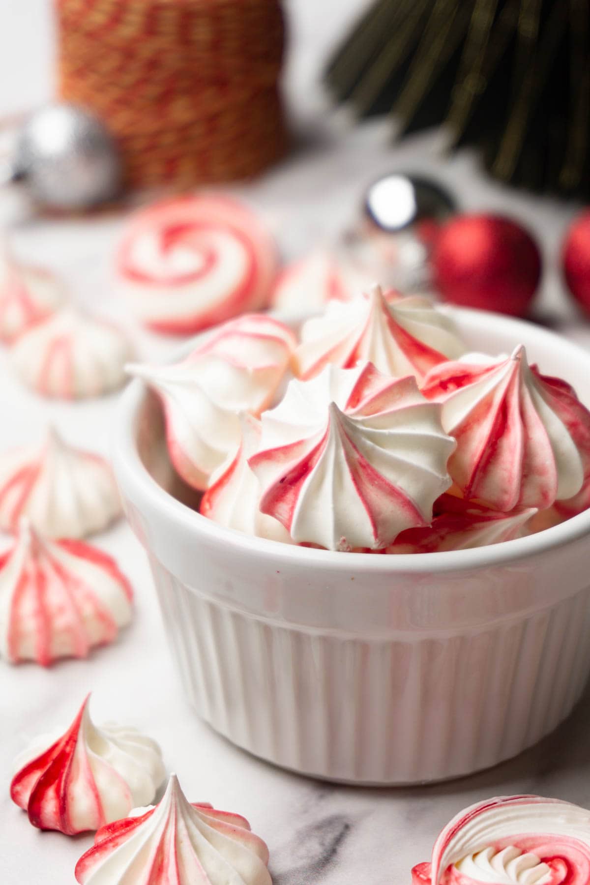 A white bowl with red and white meringue cookies, more cookies are lying around.