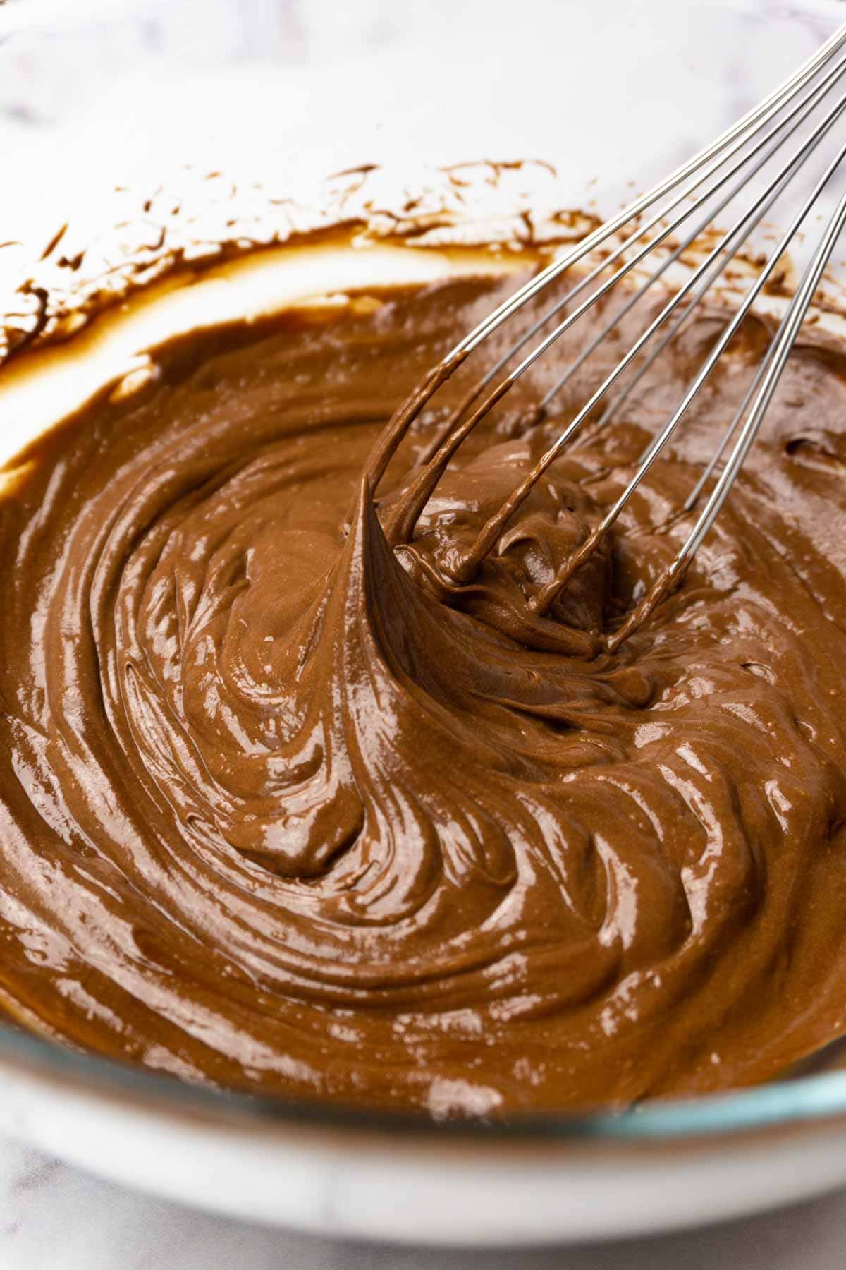 Whipped chocolate ganache in a bowl, a metal whisk is in the bowl.