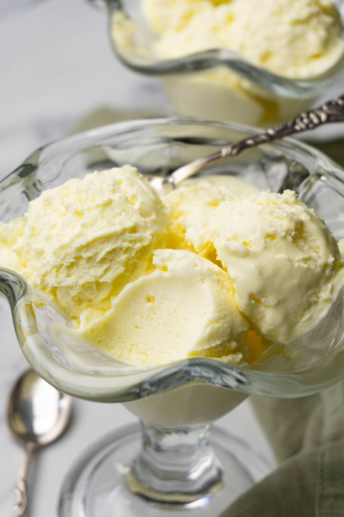 Vanilla ice cream in a glass ice cream bowl, one spoon taken.