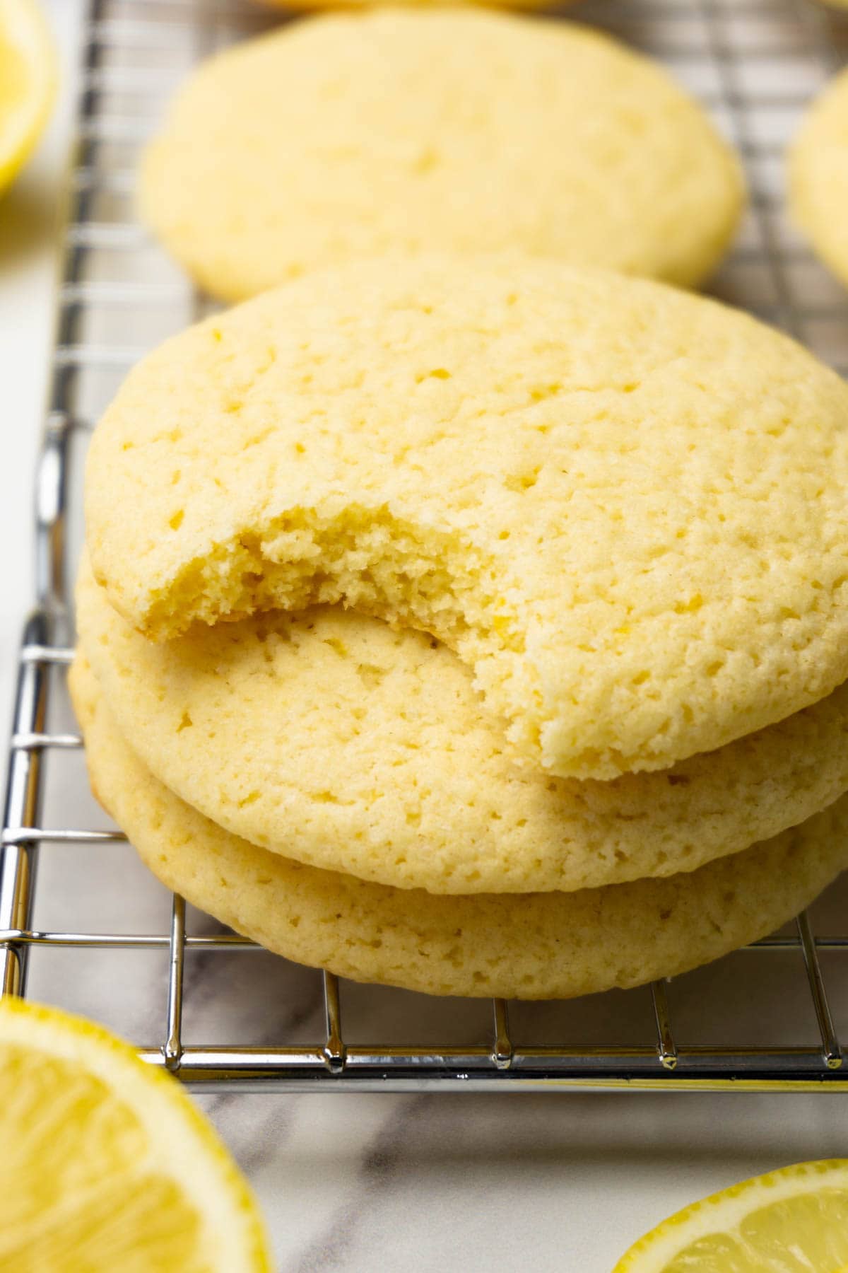 Three lemon cookies stacked on top of each other on a cooling rack, one bite taken from the top cookie.