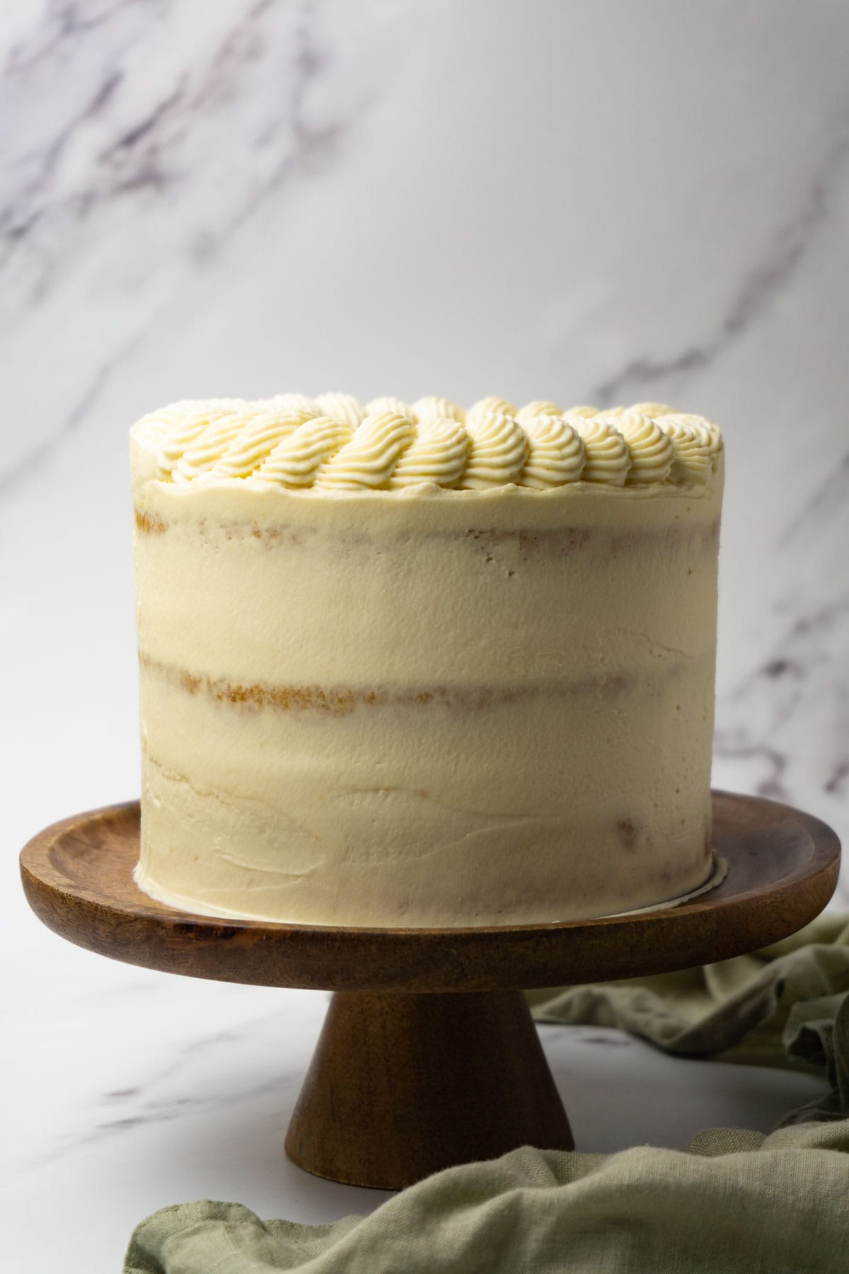 Semi-naked cake with caramel frosting on a wooden cake stand.