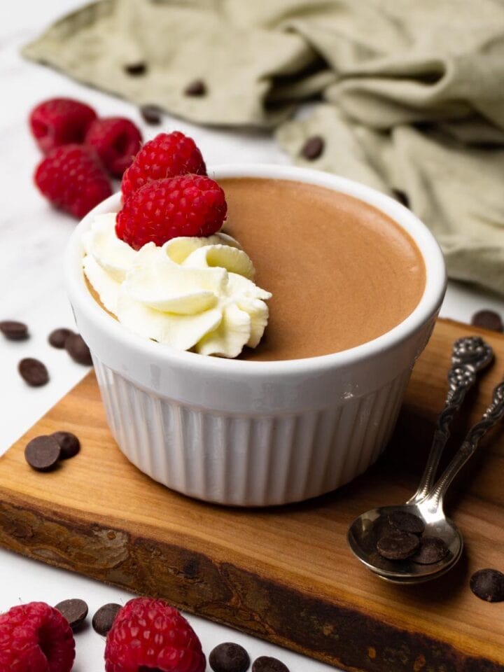 Dark chocolate mousse topped whipped cream and fresh raspberries in a white ramekin.
