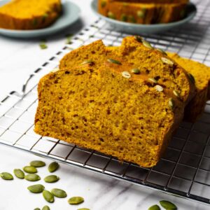 Topped with pepitas pumpkin bread slices on a cooling rack, more pepitas are lying around.