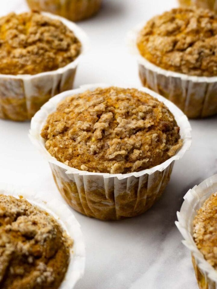 Pumpkin muffins with streusel topping in white muffin linens on a white marbled surface.