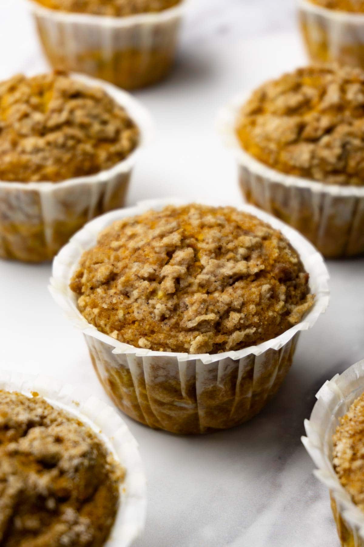 Pumpkin muffins with streusel topping in white muffin linens on a white marbled surface.