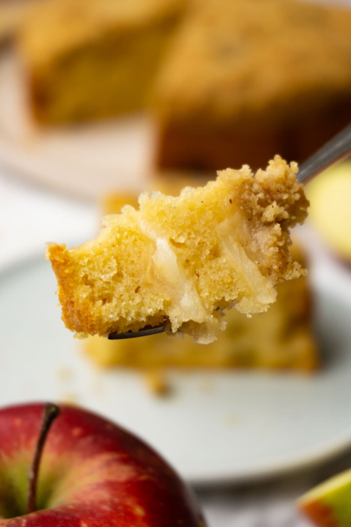 A fork with a piece of apple crumb cake on it, the rest of the cake is on the background.