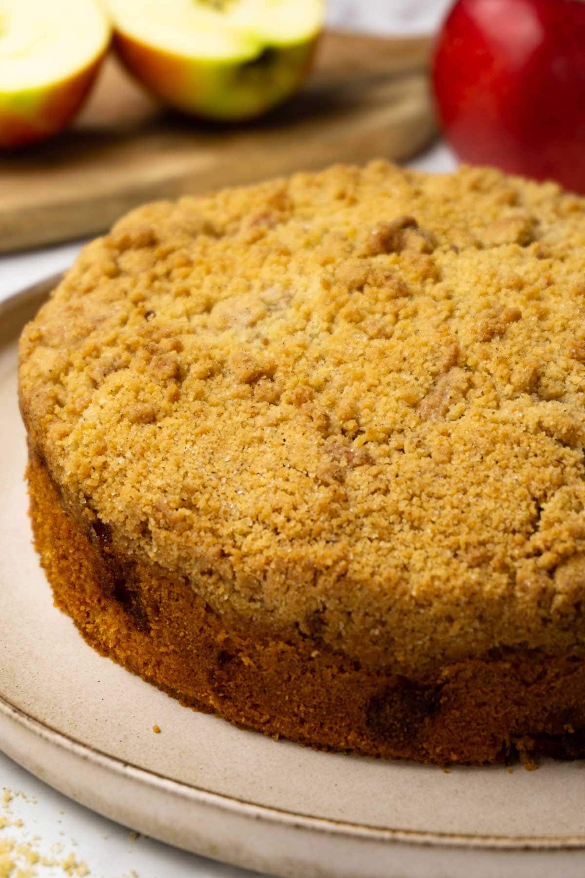 Freshly baked apple crumb cake with crunch streusel topping served on a large beige plate, fresh apples on the background.