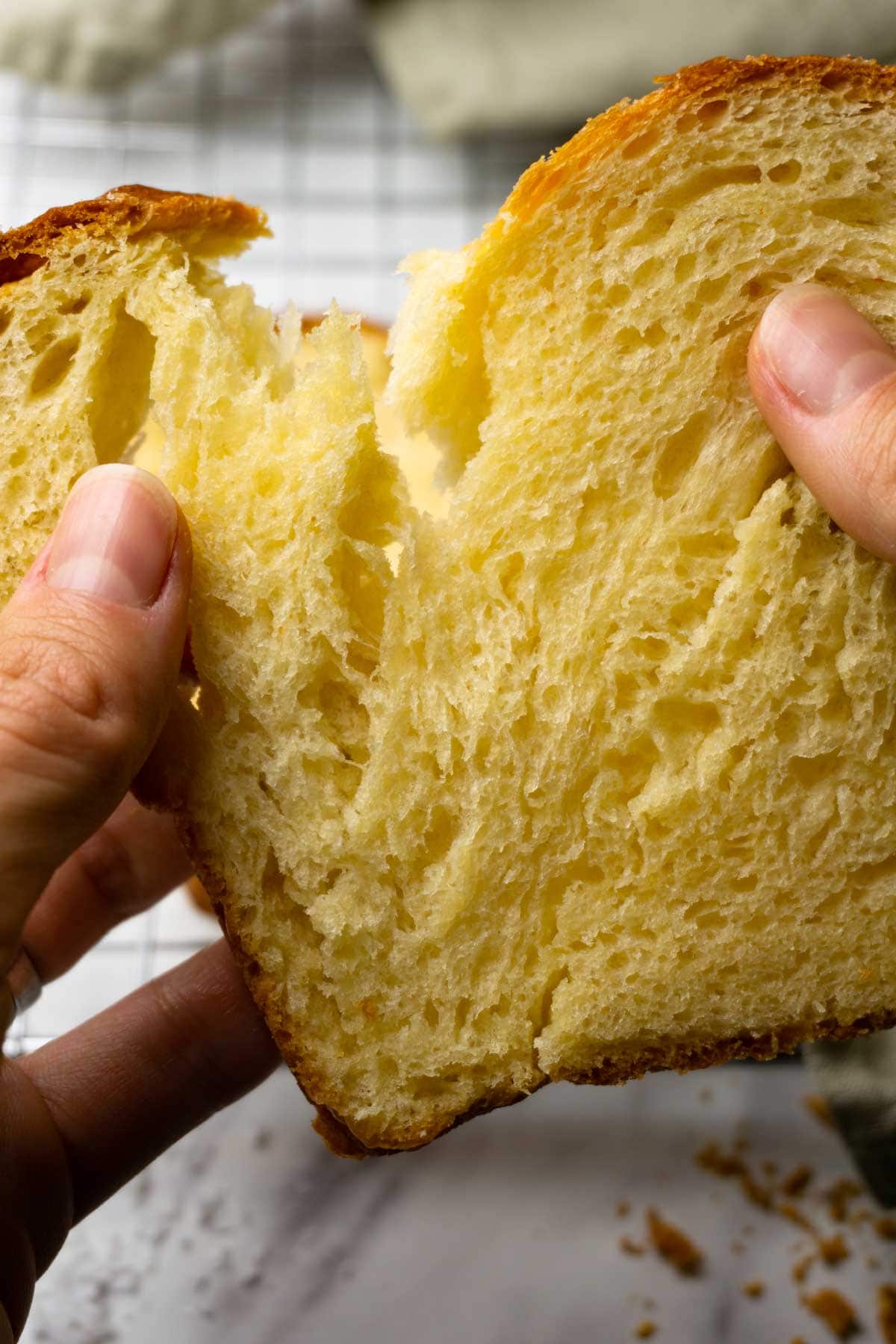 Hands rip apart a slice of freshly baked brioche bread.
