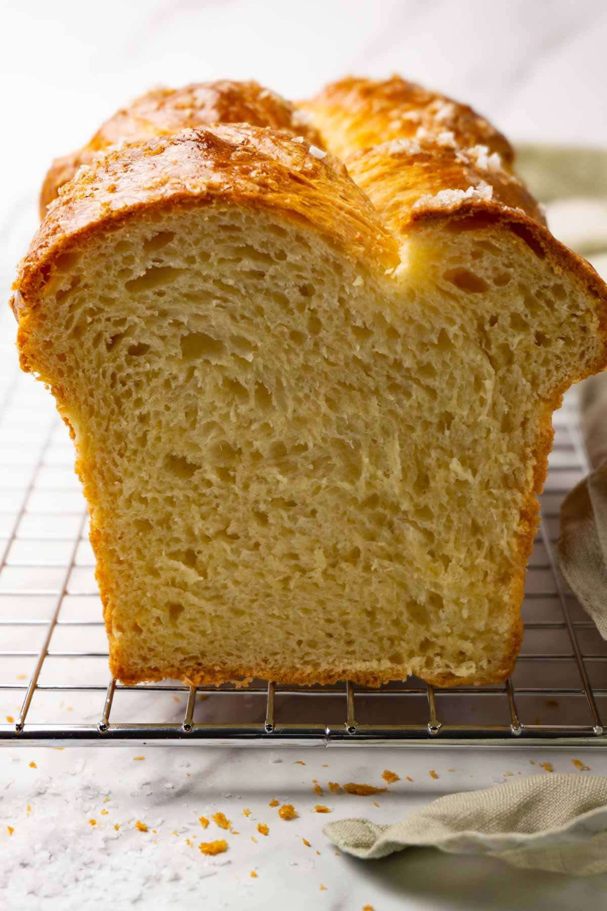 A loaf of brioche bread topped with flaky sea salt on a metal cooling rack, a slice was taken.