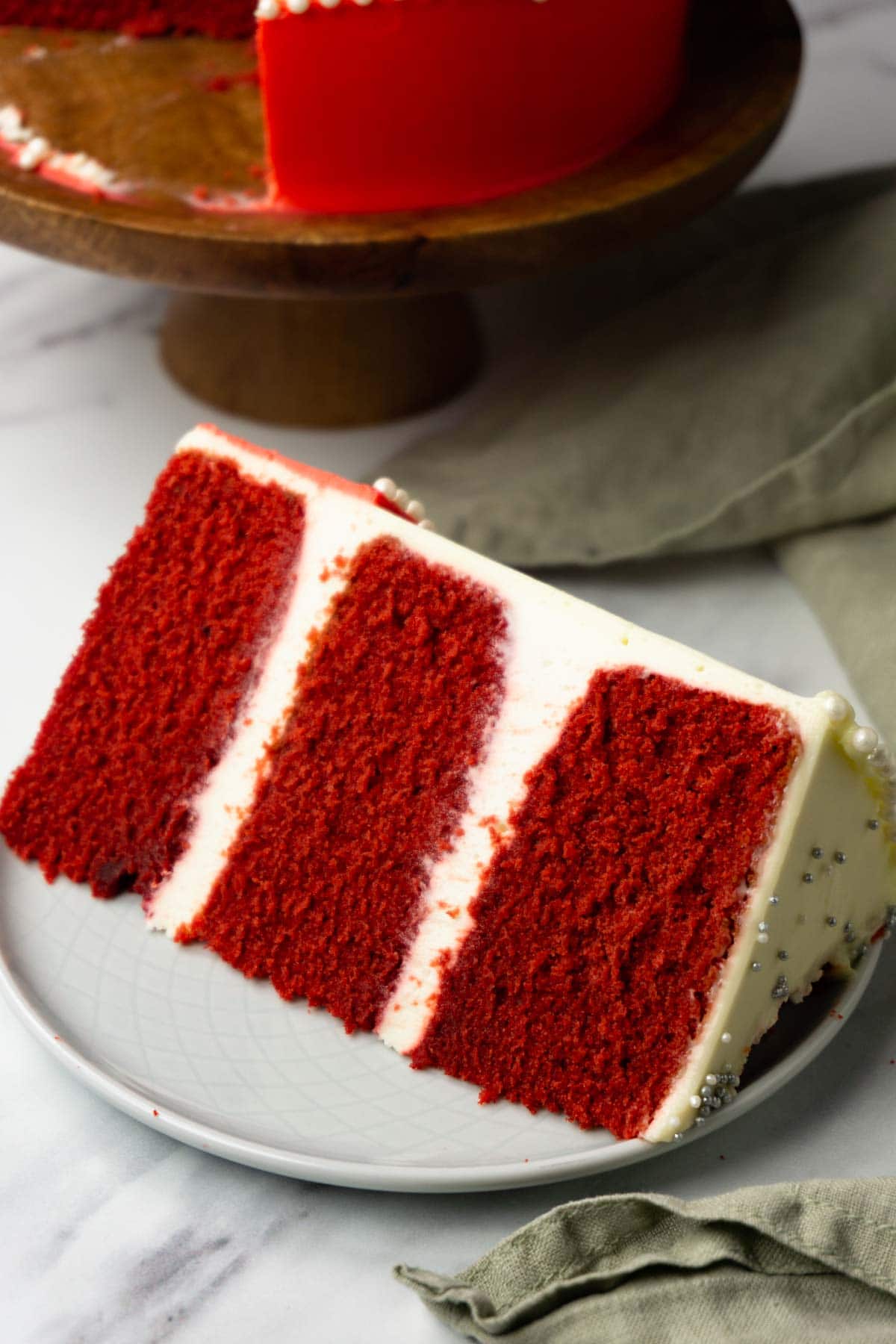 A piece of red velvet cake with white cream cheese frosting on a small round place.