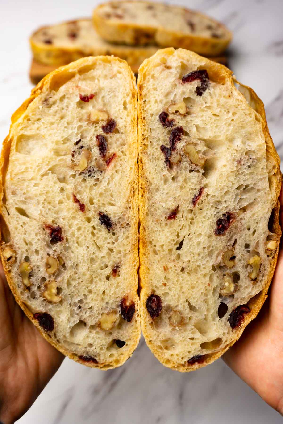A cut in half loaf of bread with walnuts and dried cranberries.