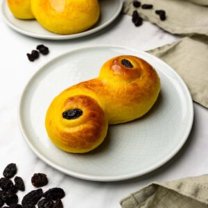 Saffron bun with raisins on a small round plate, more buns on the background.