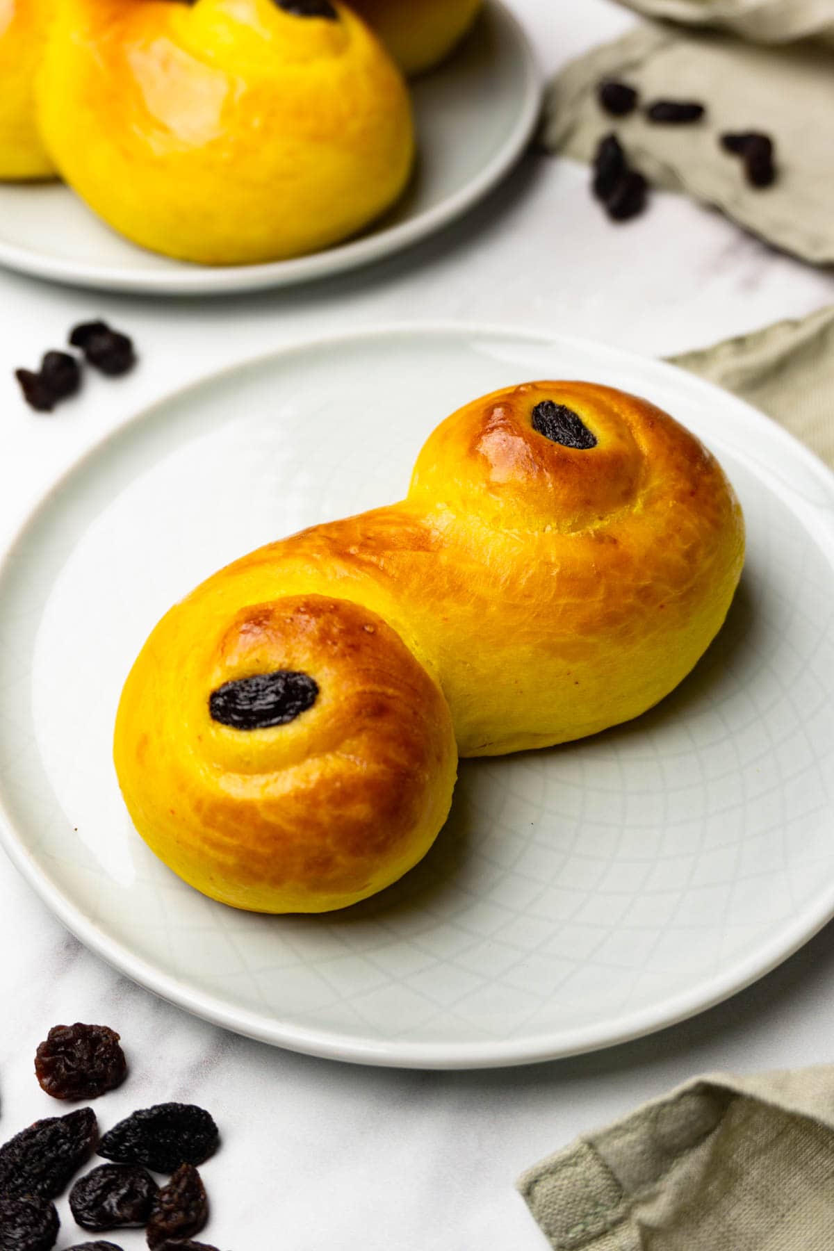 Saffron bun with raisins on a small round plate, more buns on the background.