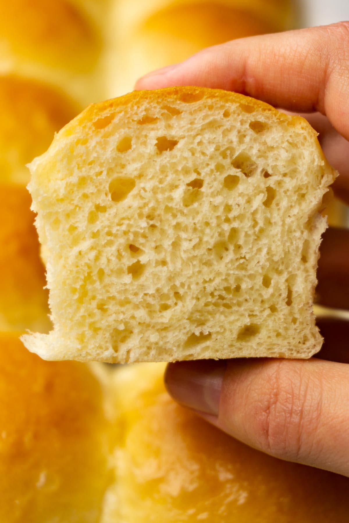 A hand is holding a cut in half soft dinner roll, more rolls on the background.