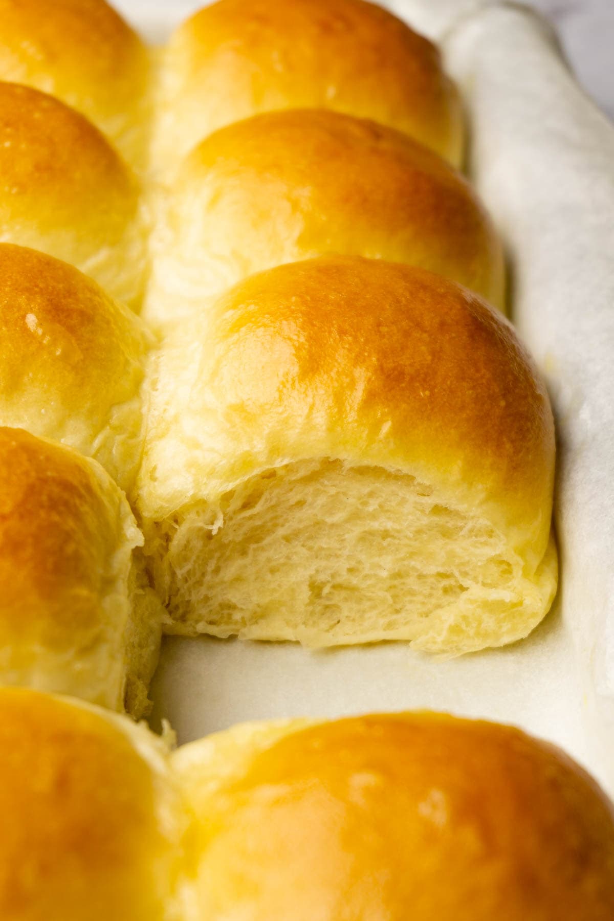 A baking pan filled with freshly-baked dinner rolls, one roll is taken.