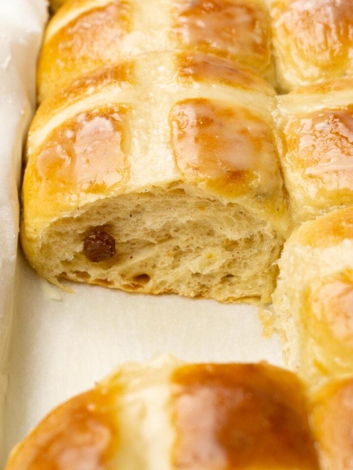 A baking dish filled with glazed hot cross buns, one bun is taken.