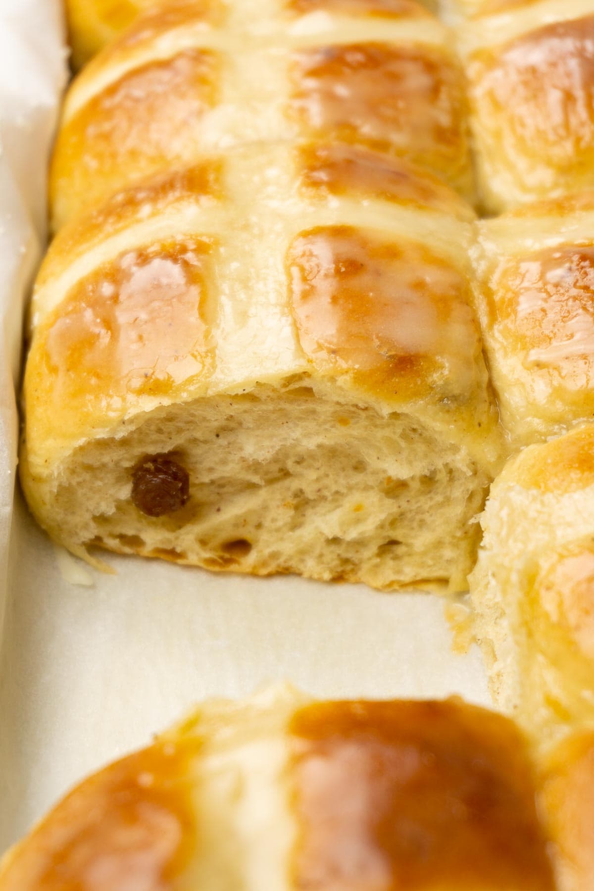 A baking dish filled with glazed hot cross buns, one bun is taken.