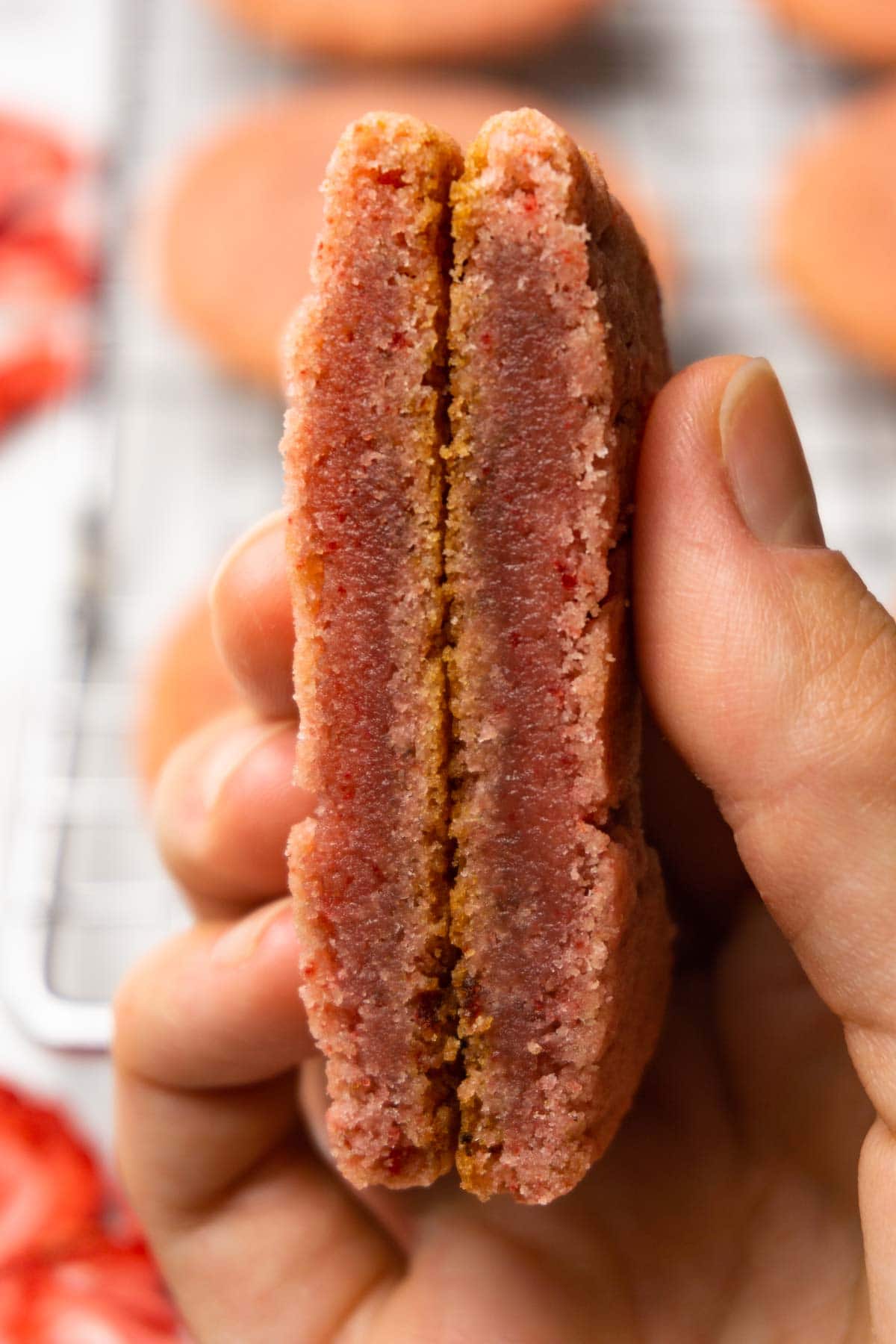 A hand is holding cut in half strawberry cookie.