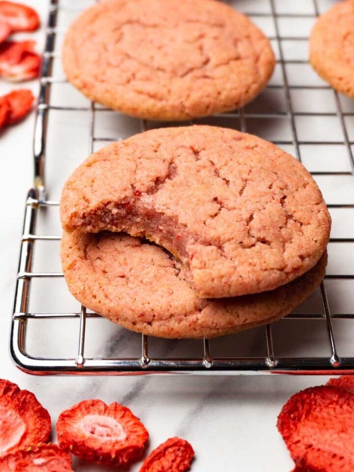 Strawberry cookies on a cooling rack, one bite is taken from one of the cookies.