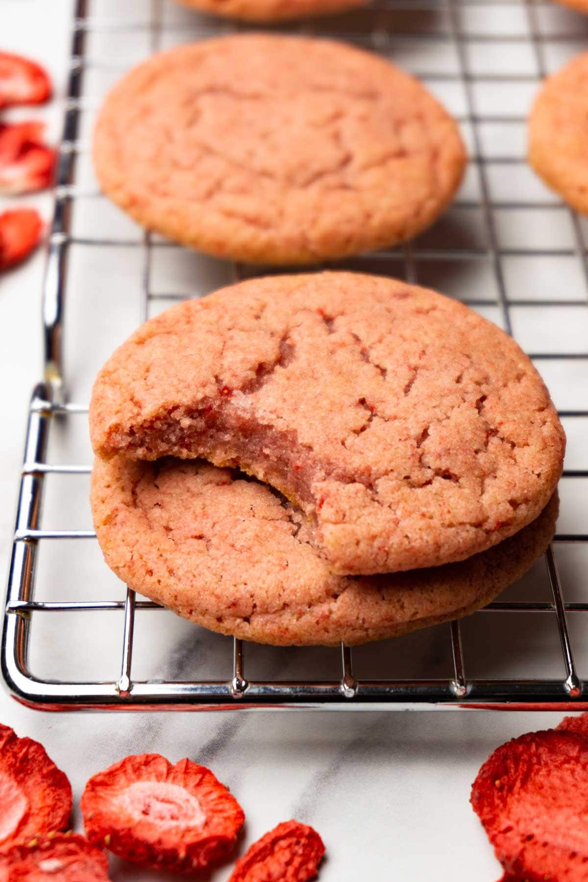 Strawberry cookies are on a cooling rack, one bite is taken from one of the cookies.