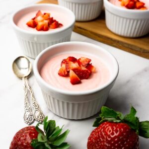 Strawberry mousse decorated with cubed fresh strawberries served in a white ramekin.