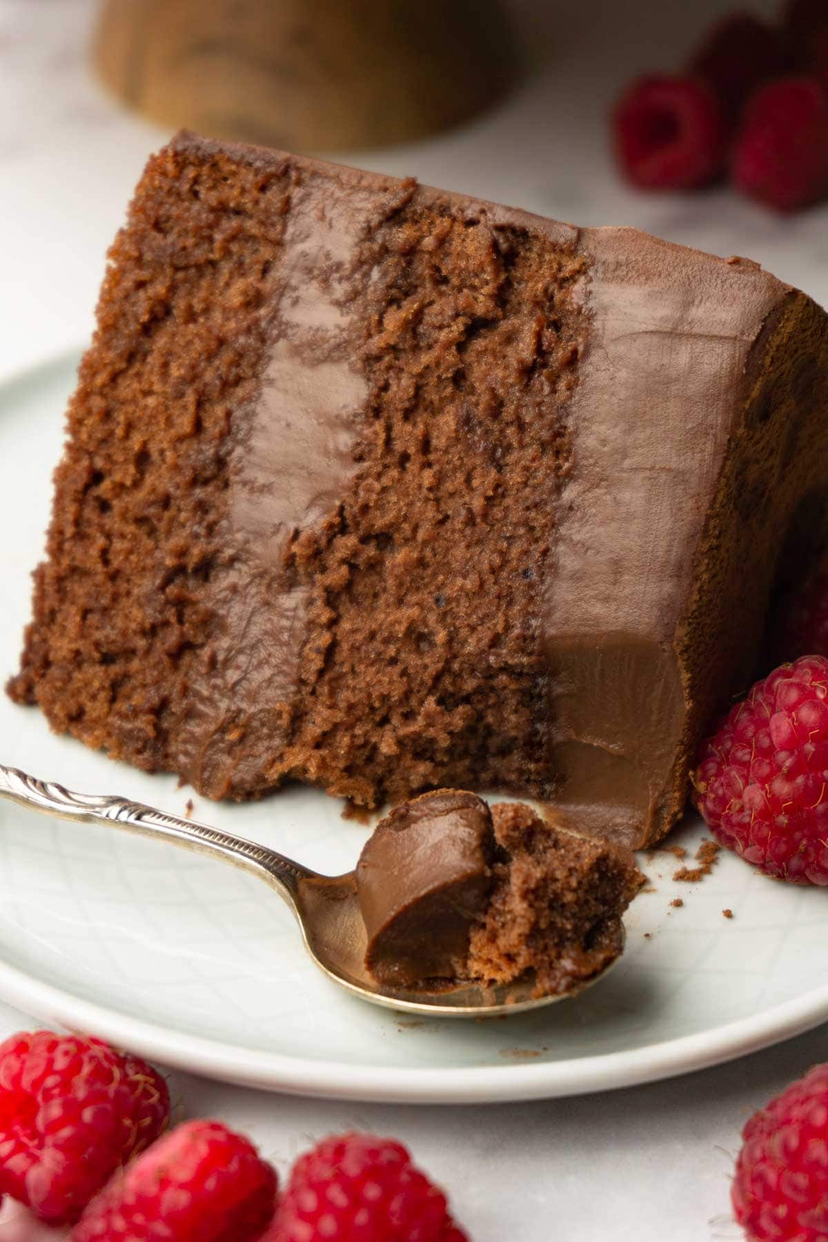 A piece of chocolate cake with chocolate mousse filling with fresh raspberries on a plate, one spoon is taken.