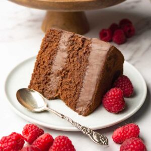 A piece of chocolate cake with chocolate mousse filling with fresh raspberries on a plate.