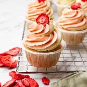 Strawberry cupcakes with cream cheese frosting decorated with freeze-dried strawberries on a metal cooling rack.