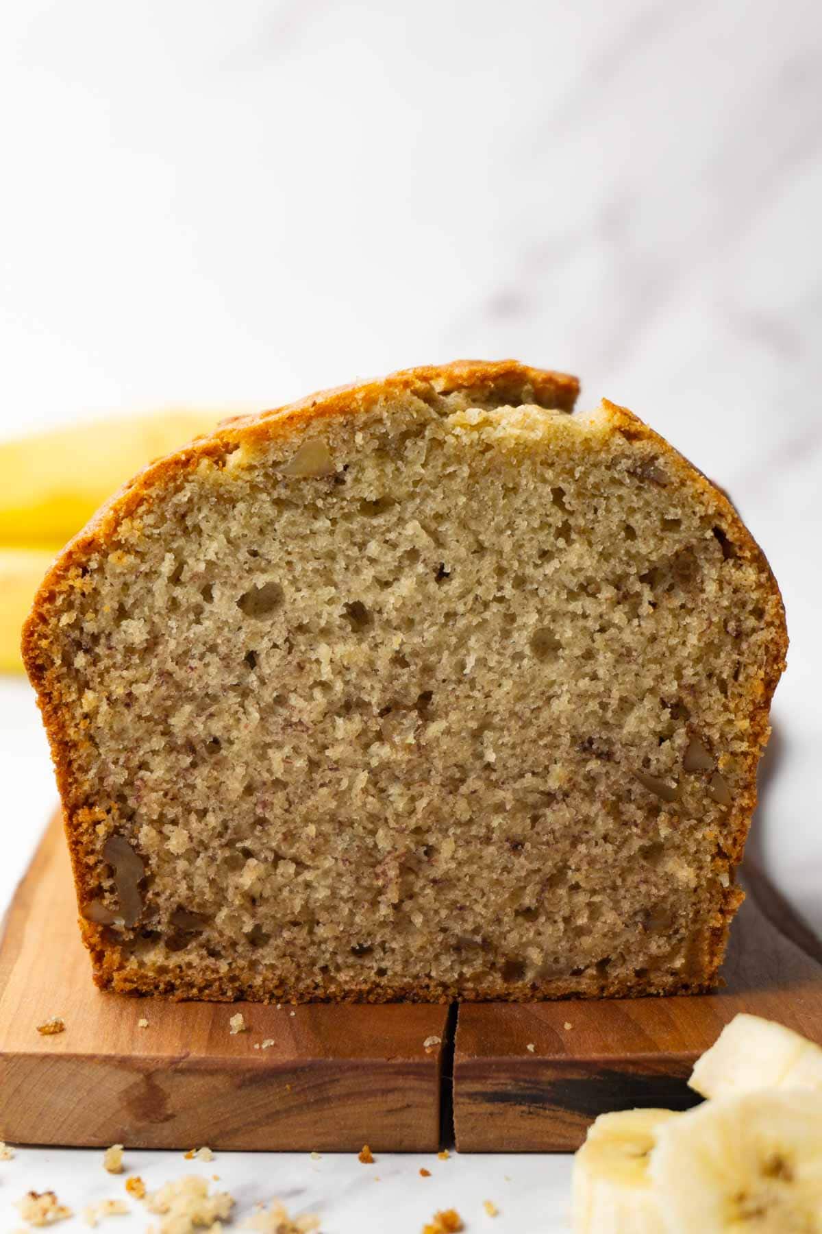 A loaf of banana bread with walnuts on a wooden cutting board; several slices were taken.