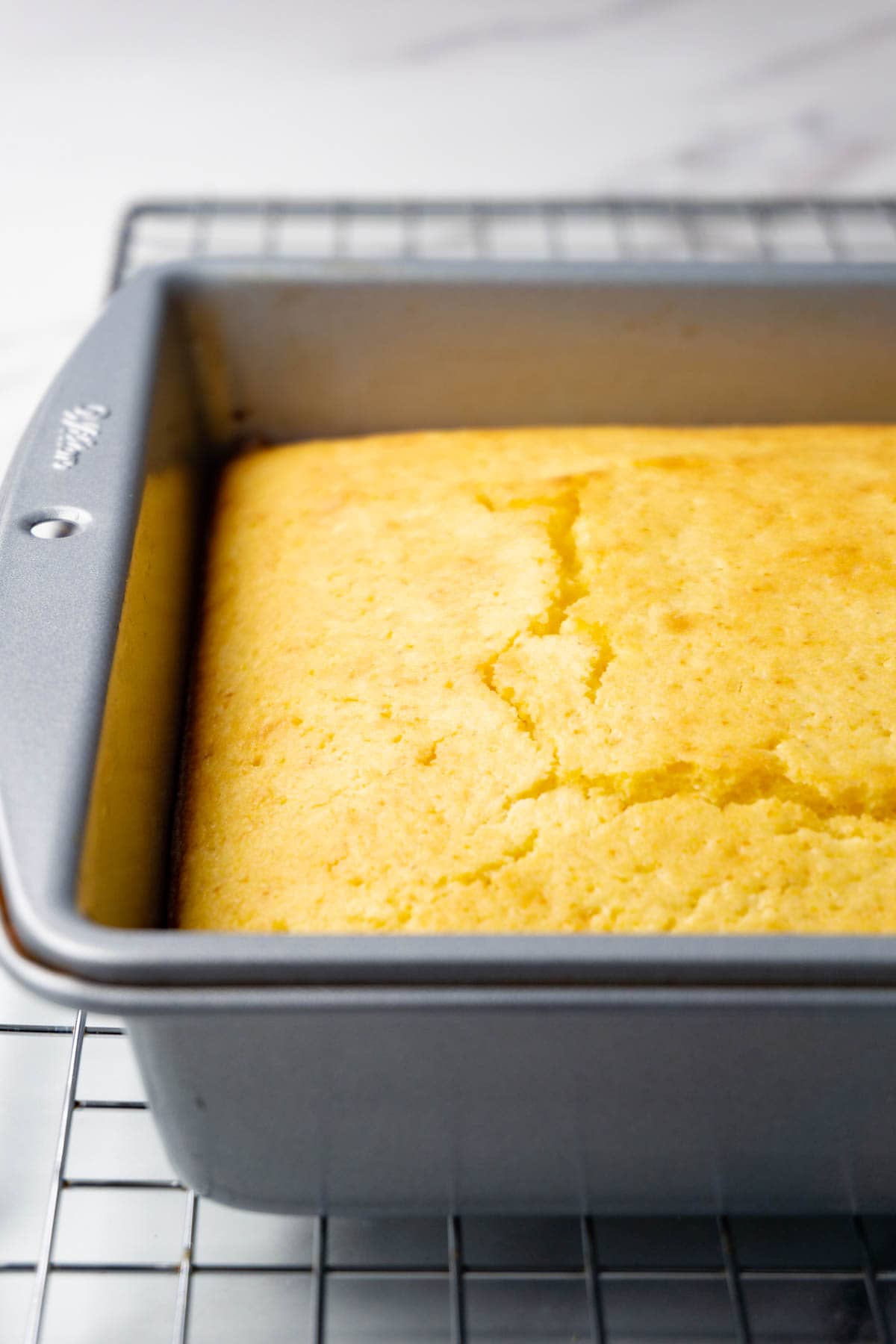 A silver baking dish with freshly-baked cornbread is standing on a wire rack.