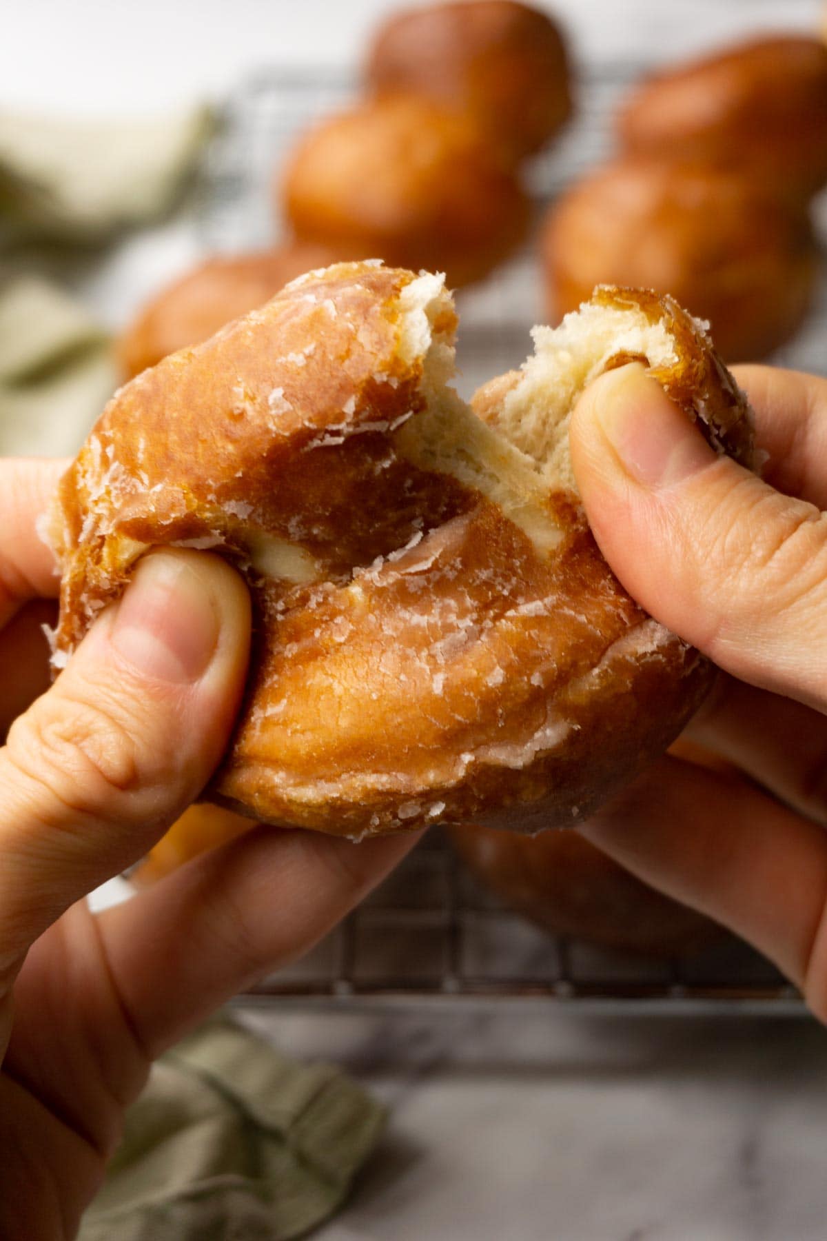 A hand is ripping apart a donut hole covered in sugar glaze.