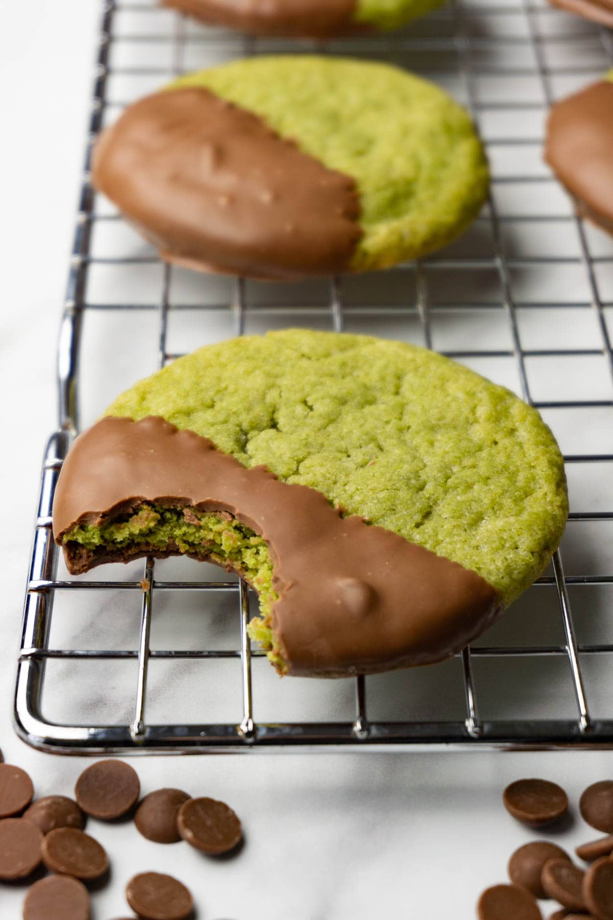 Matcha cookies with milk chocolate glaze on a cooling rack. One bite is taken from one of the cookies.