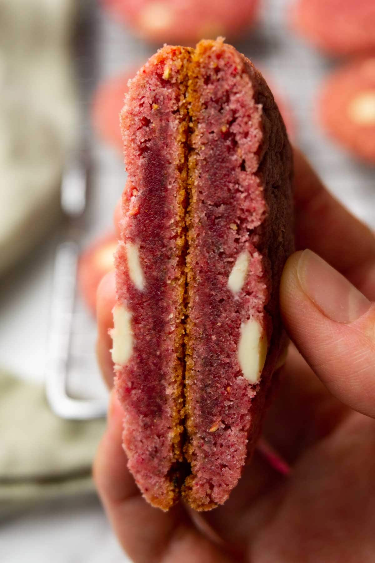 A hand is holding a cut-in-half raspberry cookie with white chocolate chips.