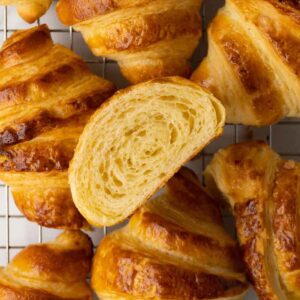 Freshly baked croissants on a metal cooling rack; one croissant is cut in half.