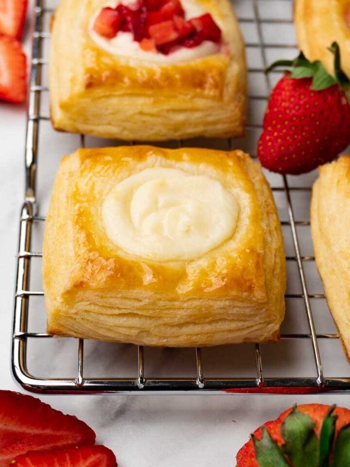 Square Danishes with cream cheese filling on a cooling rack; some Danishes have a strawberry topping.