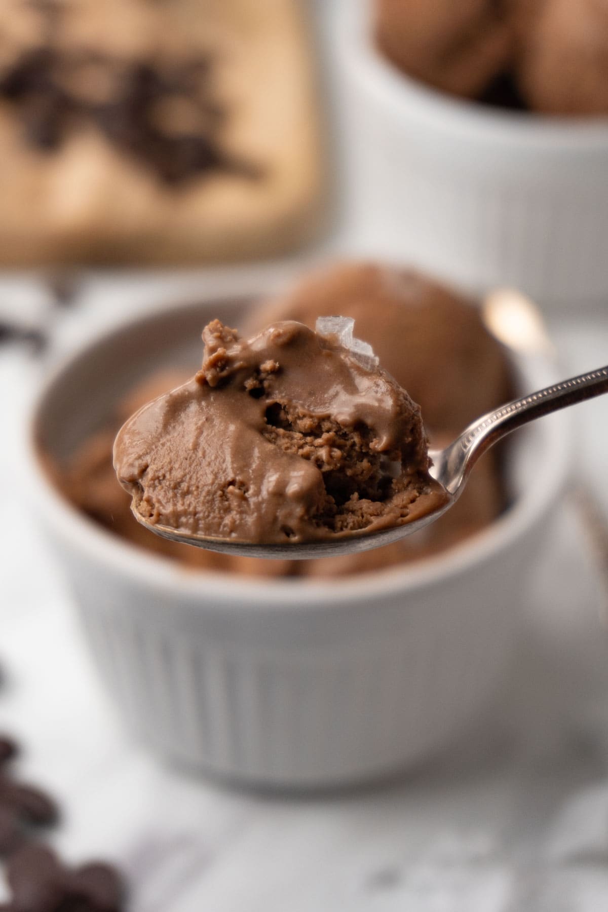 A close-up shot of a silver spoon filled with chocolate ice cream topped with sea salt flakes.
