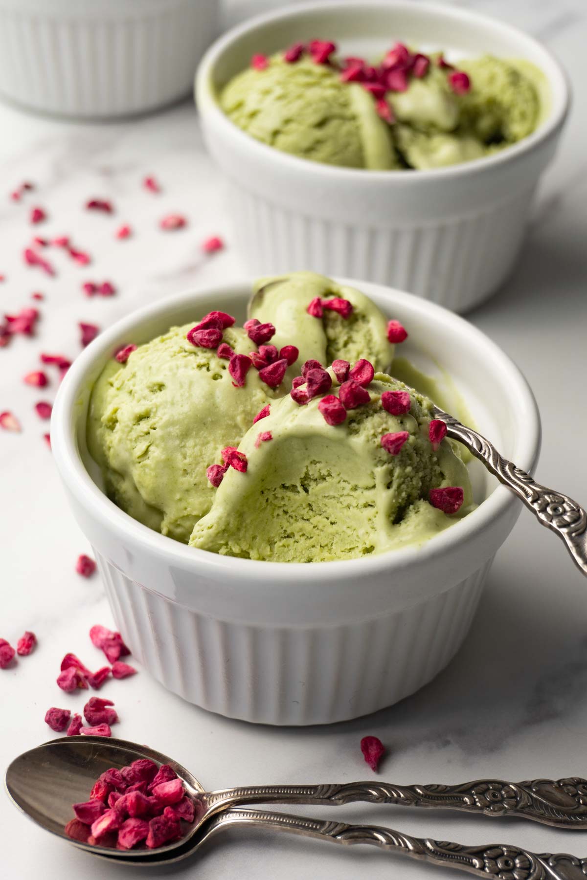 A white ramekin filled with green ice cream topped with freeze-dried raspberries; one spoon was taken