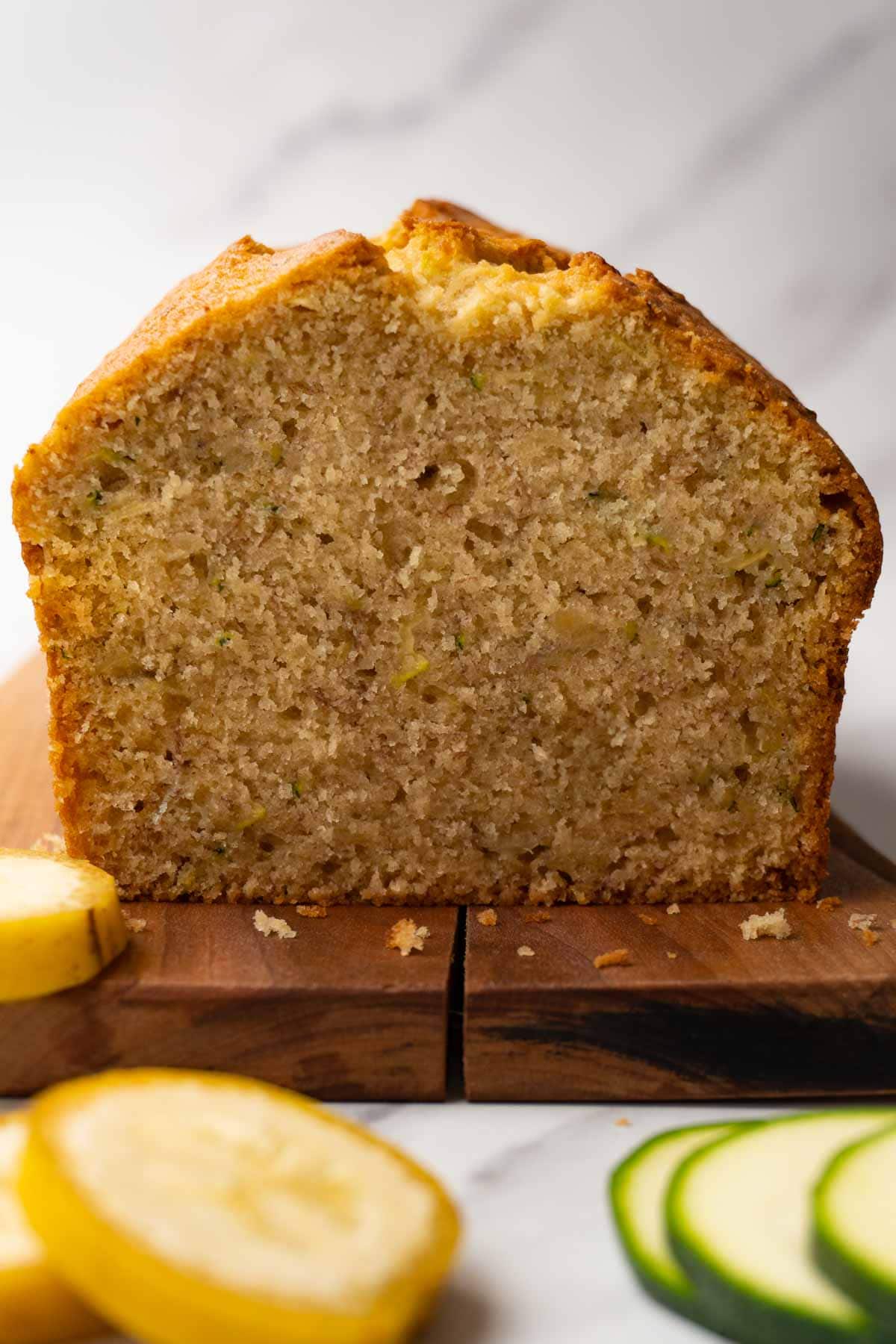 A loaf of bread with zucchini and bananas on a wooden serving board; one slice is missing.