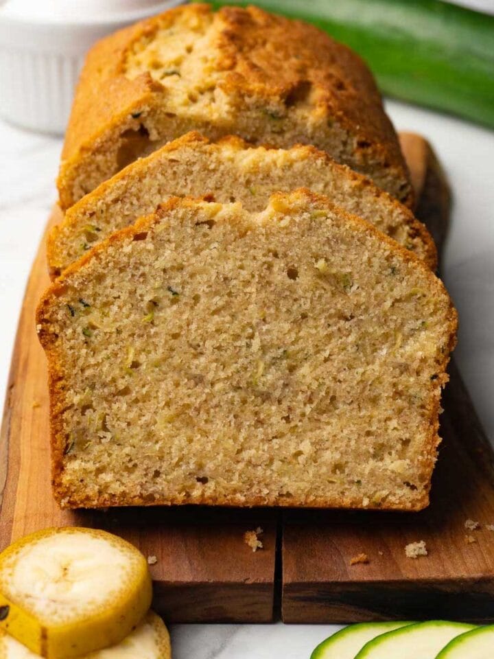 A sliced loaf of bread with zucchini and bananas on a wooden serving board.