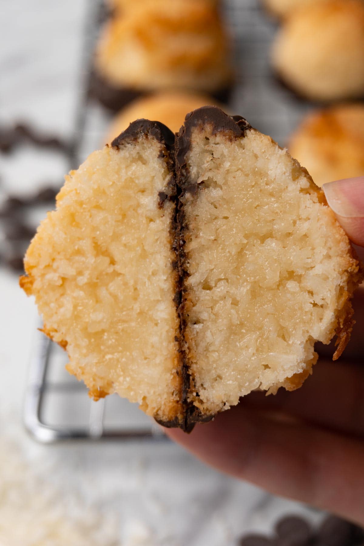 A hand is holding a cut-in-half cookie made of coconut flakes dipped in chocolate.