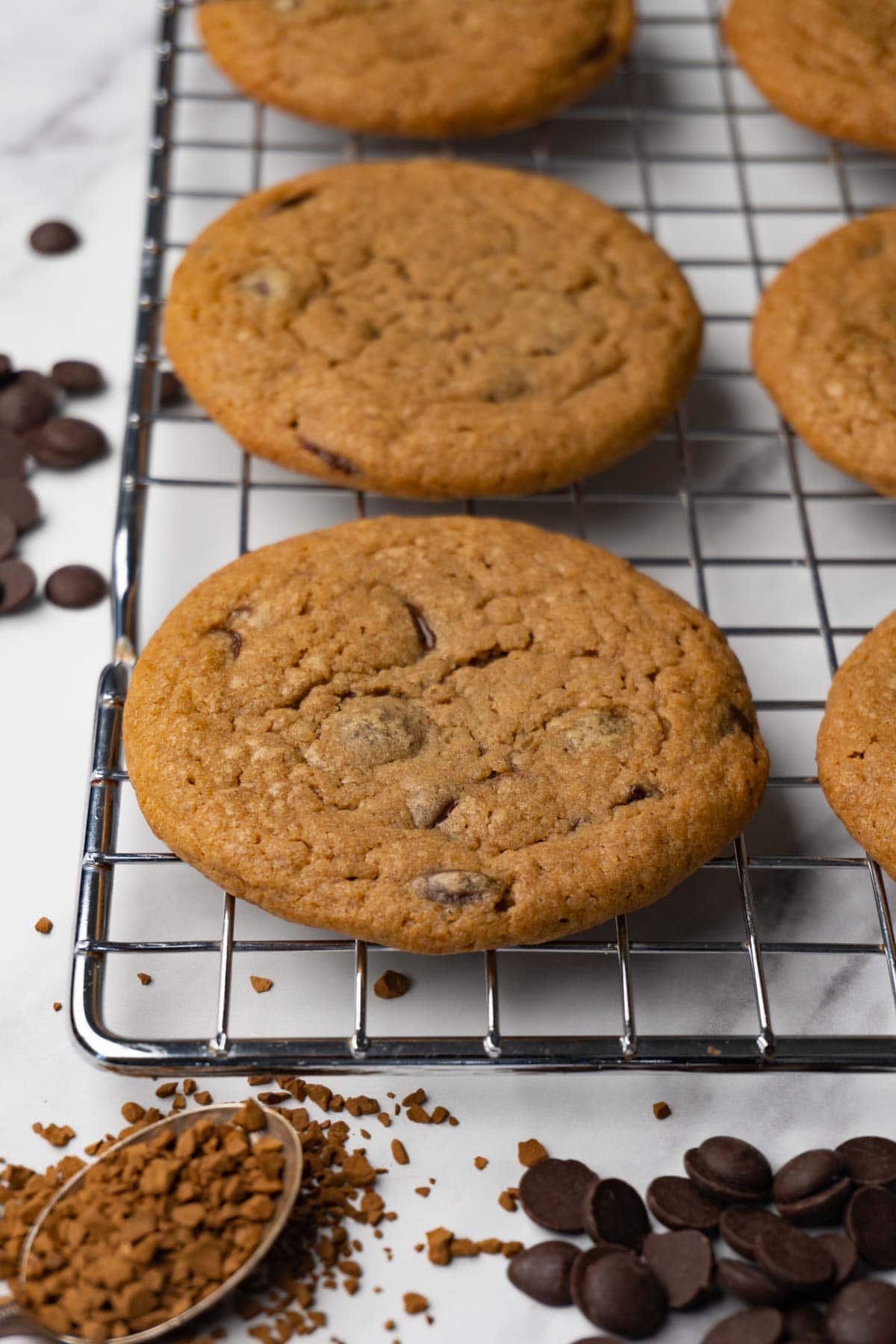 Coffee cookies with chocolate chips on a wire rack. Instant coffee granules and dark chocolate chips are lying around.