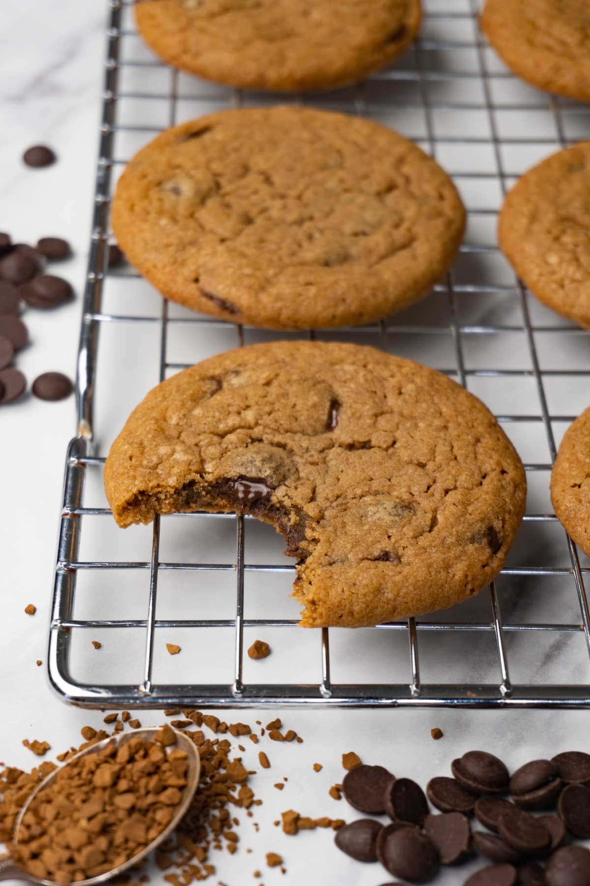 Coffee cookies with chocolate chips on a wire rack. One bite was taken from one of the cookies.