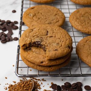 Coffee cookies with chocolate chips stacked on top of each other on a cooling rack. One bite is taken from the top cookie.