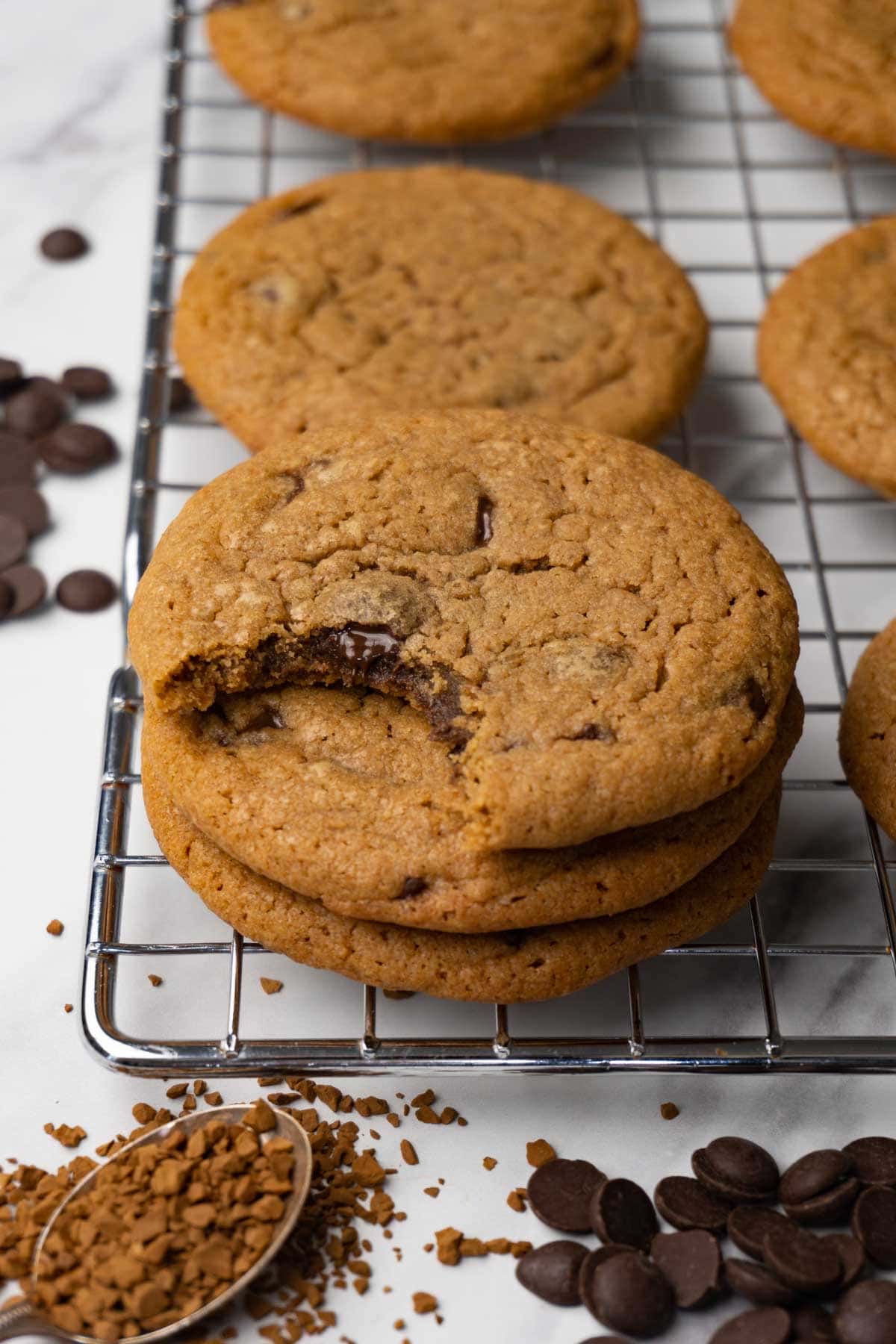 Coffee cookies with chocolate chips stacked on top of each other on a cooling rack. One bite is taken from the top cookie.