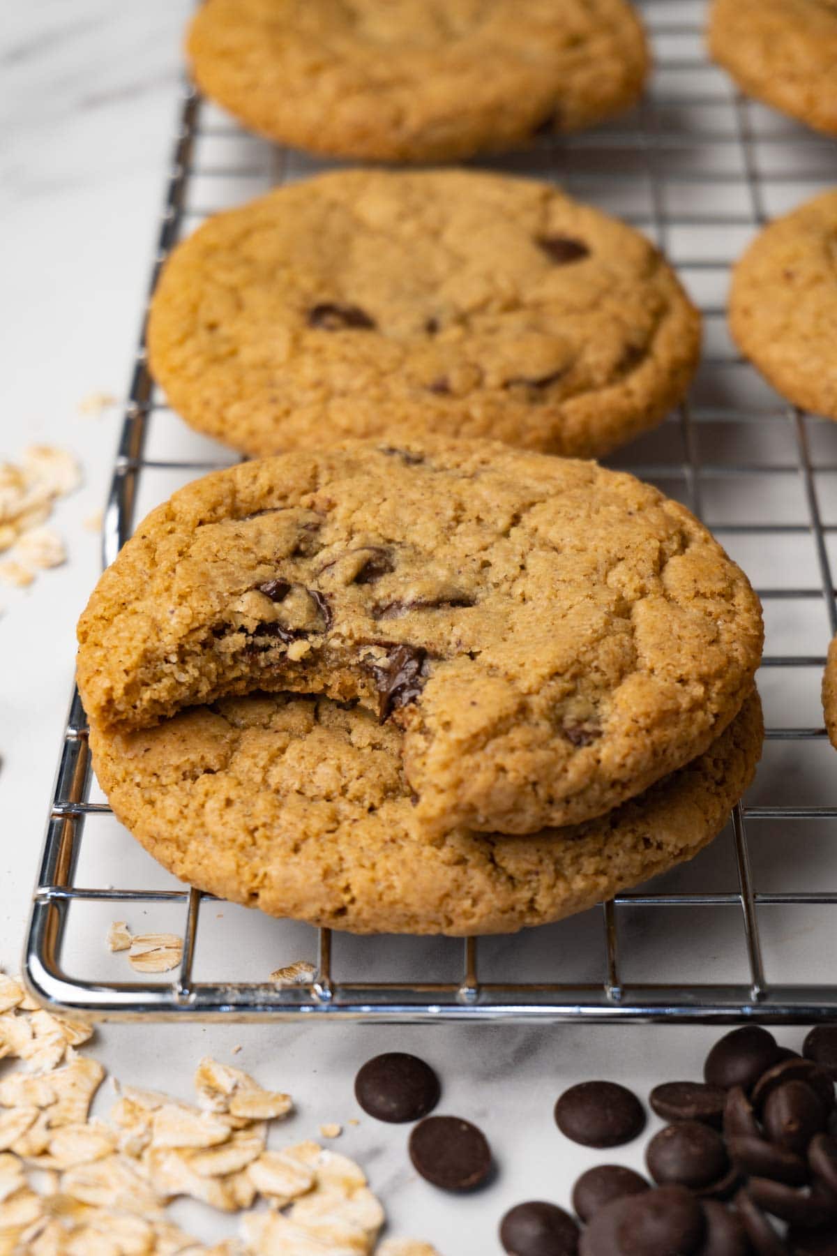 Oat flour cookies with chocolate chips stacked on top of each other on a cooling rack. One bite is taken from the top cookie.