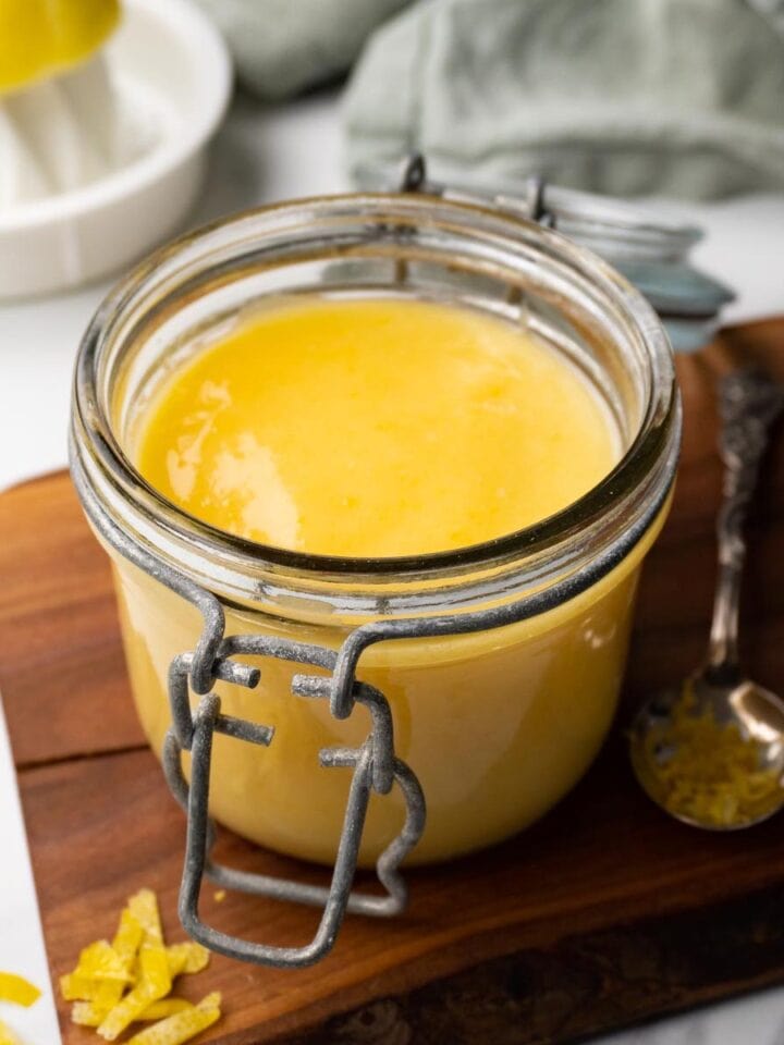A glass jar filled with lemon curd is standing on a wooden board.