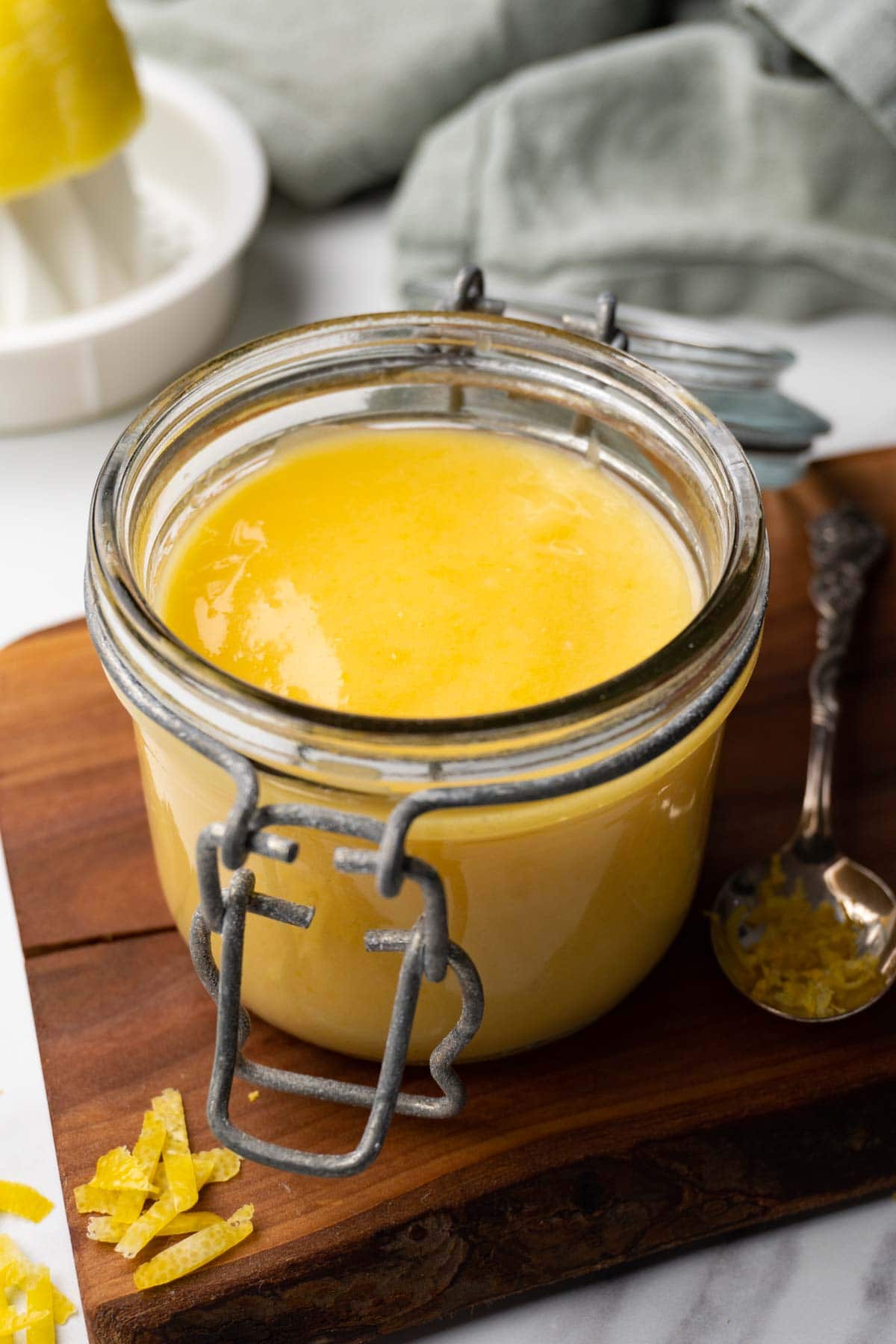A glass jar filled with lemon curd is standing on a wooden board.